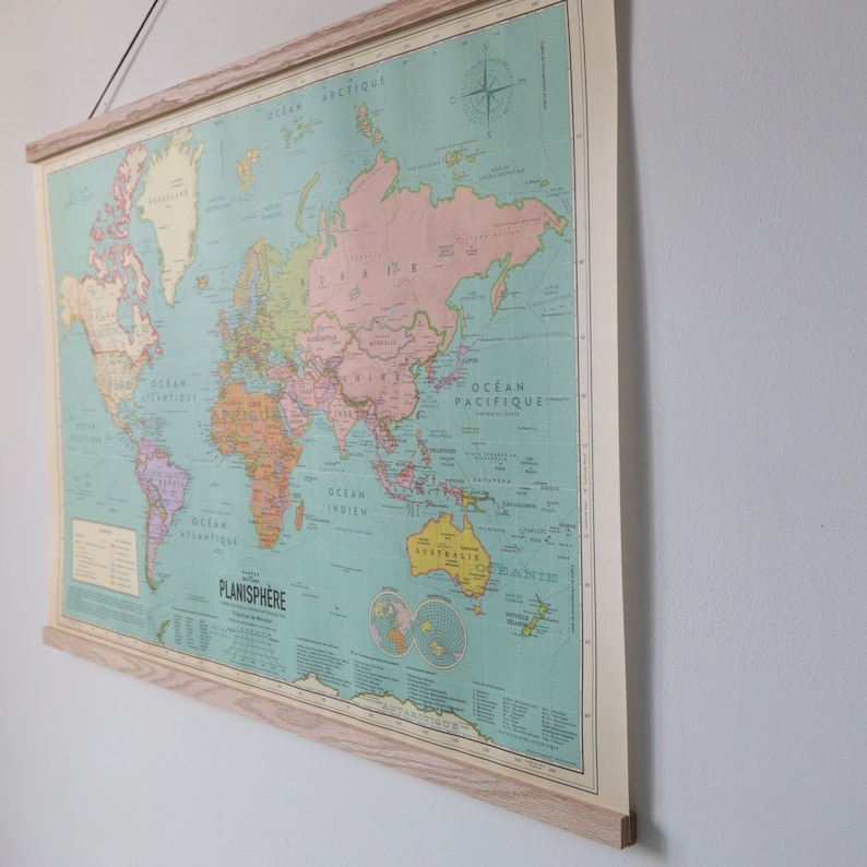 K&ouml;nnte beinhalten: Eine Vintage-Weltkarte in einem Holzrahmen. Die Karte ist auf einem hellblauen Hintergrund mit braunen, orangen und rosafarbenen Kontinenten gedruckt. Die Karte tr&auml;gt den Titel "Planisphere" und enth&auml;lt die W&ouml;rter "Ocean Atlantique", "Ocean Pacifique" und "Ocean Indien".