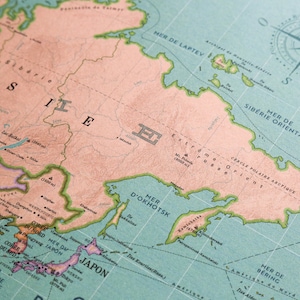 Op de afbeelding: Een vintage wereldkaart met een lichtblauwe achtergrond en groene en bruine lijnen. De kaart toont het oostelijke deel van Rusland, inclusief de Zee van Ochotsk, de Laptevzee en de Beringzee. De kaart is in het Frans en Engels gelabeld.