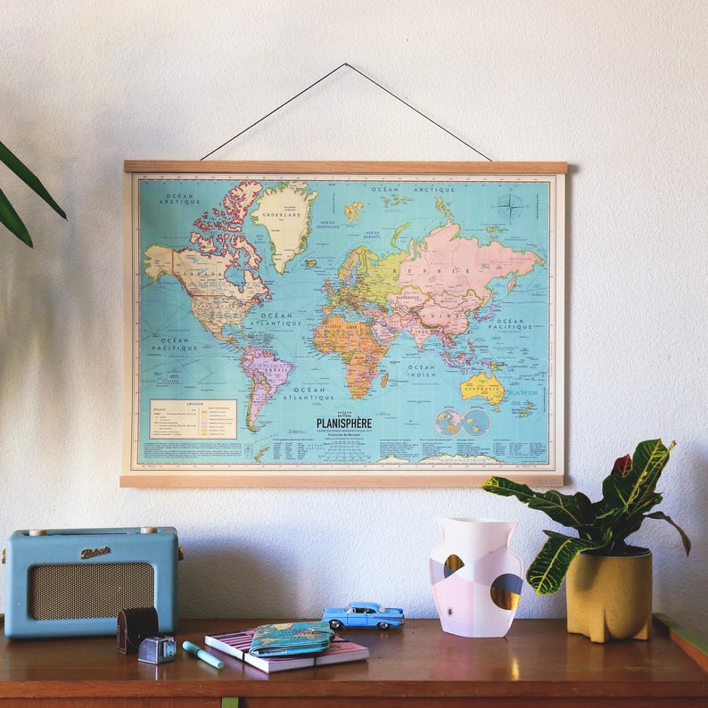 K&ouml;nnte beinhalten: Ein Vintage-Weltkarten-Druck mit blauem Hintergrund und bunten Kontinenten. Die Karte ist mit einem Holzrahmen gerahmt und h&auml;ngt an einer wei&szlig;en Wand. Die Karte tr&auml;gt den Titel "PLANISPHERE".