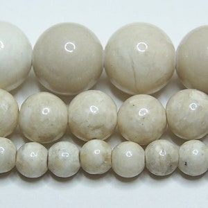 May include: A strand of white fossilized coral beads in various sizes. The beads are round and have a smooth, polished finish.