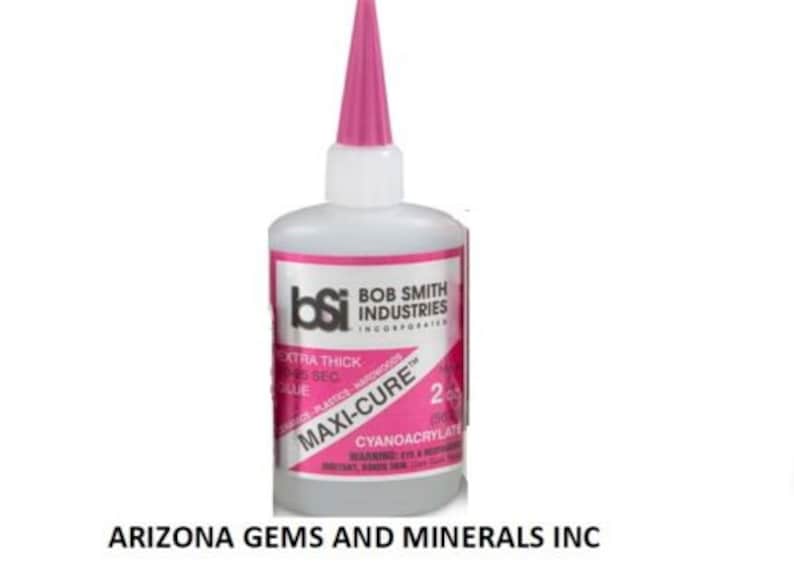 May include: A pink bottle of Bob Smith Industries Maxi-Cure Extra Thick 25 Second Glue. The bottle is labeled with the brand name, product name, and instructions for use. The bottle is 2 oz.