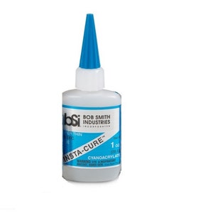 May include: A 1 ounce bottle of Bob Smith Industries Insta-Cure cyanoacrylate adhesive. The bottle is clear and has a blue cap with a pointed tip. The label is blue and white and says "Insta-Cure" in large letters. The label also includes a warning about eye and respiratory irritation.