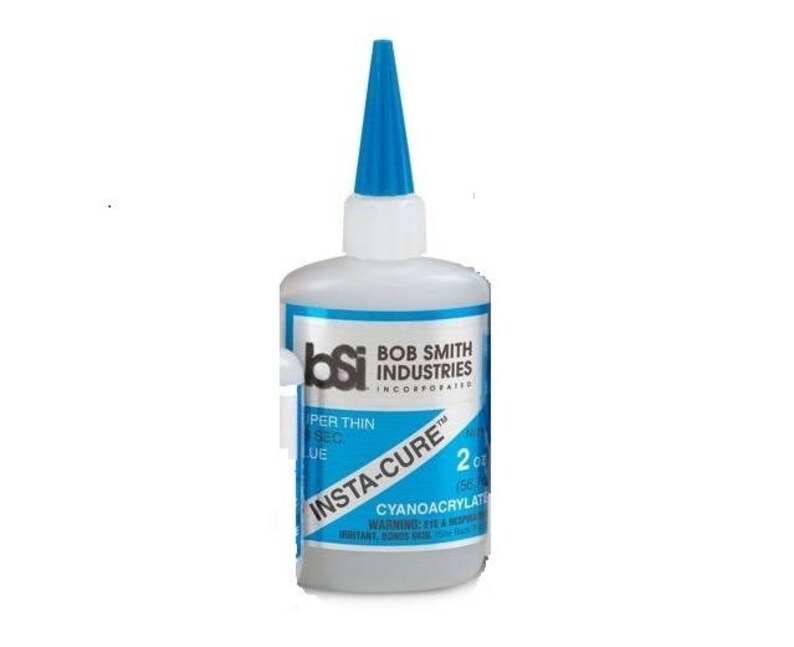 May include: A blue bottle of Bob Smith Industries Insta-Cure super thin cyanoacrylate glue. The bottle is labeled with the text "Insta-Cure" and "2 oz (56 g)".
