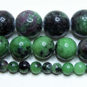 May include: A strand of green, black, and pink gemstone beads. The beads are round and have a smooth, polished finish. The beads are arranged in three rows, with the largest beads in the top row and the smallest beads in the bottom row.