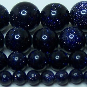 May include: Close-up of several strands of dark blue aventurine gemstone beads. The beads vary in size and have a sparkling, glittery appearance. The beads are round and polished, reflecting light.