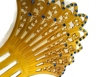May include: A gold plastic hair comb with a decorative design and blue rhinestones.