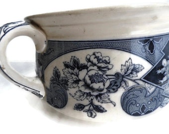 May include: A white ceramic chamber pot with a blue and white floral design. The pot has a handle and a wide, round opening.