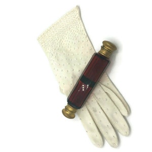 May include: A vintage glass perfume bottle with a gold top and a dark red liquid inside. The bottle is lying on top of a white glove with small white dots.