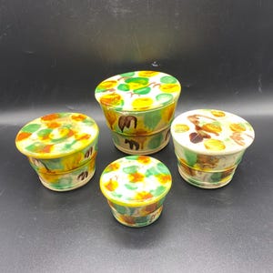 May include: Set of four ceramic containers with lids. The containers are decorated with a colorful abstract pattern of green, yellow, orange, and brown. The containers are of varying sizes.