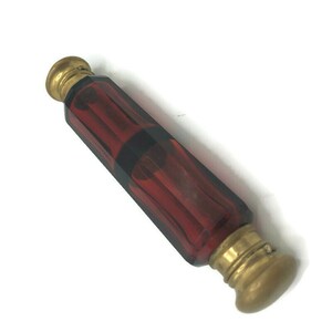 May include: A vintage glass bottle with a dark red hue and gold metal caps. The bottle has a faceted design and is likely used for perfume or essential oils.