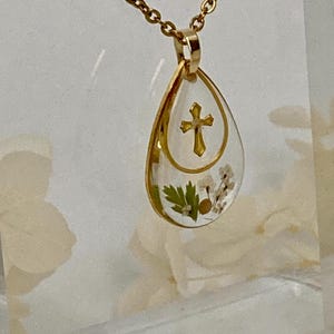 Pu&ograve; includere: Collana con pendente dorato con un pendente in resina a forma di goccia. Il pendente presenta un design a croce dorata e fiori secchi. La catena della collana &egrave; anch'essa dorata. Il pendente &egrave; lungo circa 3,8 cm.