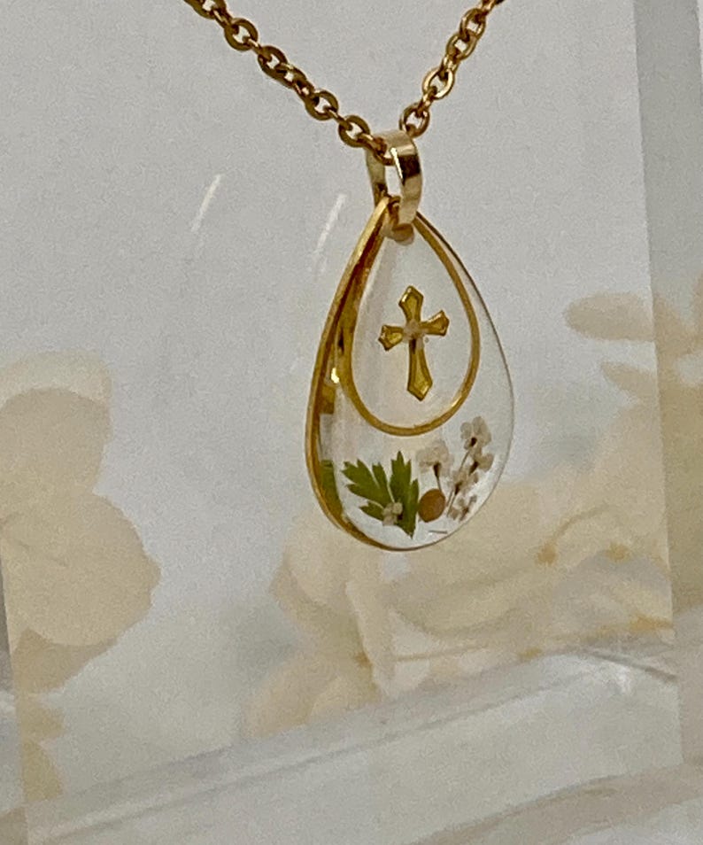 Pu&ograve; includere: Collana con pendente dorato con un pendente in resina a forma di goccia. Il pendente presenta un design a croce dorata e fiori secchi. La catena della collana &egrave; anch'essa dorata. Il pendente &egrave; lungo circa 3,8 cm.