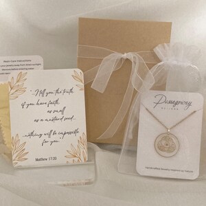 K&ouml;nnte beinhalten: Eine goldfarbene Halskette mit rundem Anh&auml;nger, pr&auml;sentiert mit einer Geschenkbox, einer Karte mit Text und einem kleinen Beutel. Auf der Karte steht: "Wahrlich, ich sage euch: Wenn ihr Glauben habt wie ein Senfkorn... so wird euch nichts unm&ouml;glich sein."