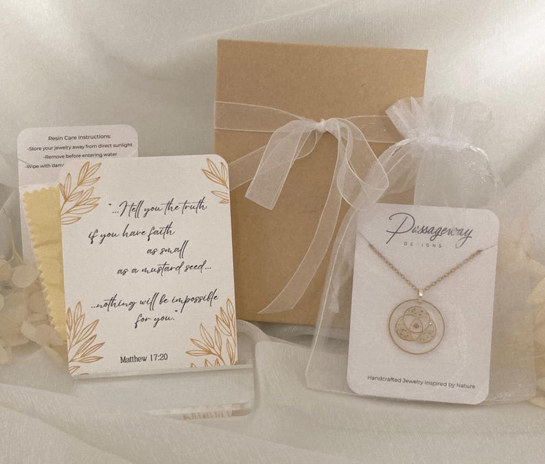 K&ouml;nnte beinhalten: Eine goldfarbene Halskette mit rundem Anh&auml;nger, pr&auml;sentiert mit einer Geschenkbox, einer Karte mit Text und einem kleinen Beutel. Auf der Karte steht: "Wahrlich, ich sage euch: Wenn ihr Glauben habt wie ein Senfkorn... so wird euch nichts unm&ouml;glich sein."