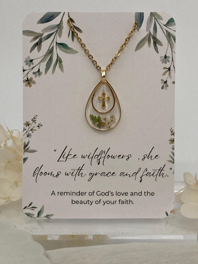 Pu&ograve; includere: Collana dorata con un ciondolo a goccia contenente una piccola croce e fiori secchi. La collana &egrave; appesa a una carta con la citazione "Come i fiori selvatici, fiorisce con grazia e fede."