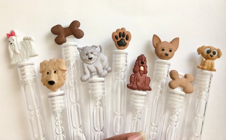 May include: A set of ten clear plastic bubble wands with various dog-themed toppers. The toppers include a paw print, a bone, a brown dog, a white dog, a brown and white dog, a chihuahua, a golden retriever, and a Maltese.