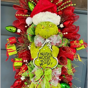 May include: A Grinch Christmas wreath with red and green mesh, a plush Grinch figure wearing a Santa hat, and a sign that says "The Noise! Noise! Noise! Noise!"