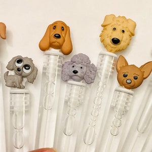 May include: A set of ten clear plastic bubble wands with different dog-shaped toppers. The toppers are made of plastic and feature various dog breeds, including a poodle, a chihuahua, a dachshund, and a golden retriever.