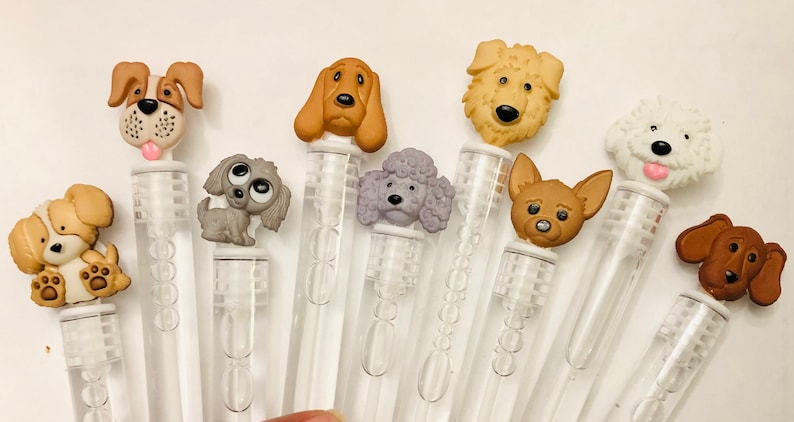 May include: A set of ten clear plastic bubble wands with different dog-shaped toppers. The toppers are made of plastic and feature various dog breeds, including a poodle, a chihuahua, a dachshund, and a golden retriever.