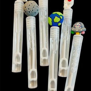 May include: A collection of clear plastic bubble wands with various space-themed toppers. The toppers include a rocket ship, a moon, an astronaut, a planet Earth, a bunny astronaut, and a UFO with a bear.