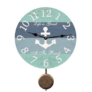 May include: A round wall clock with a nautical theme. The clock face is divided into blue and teal horizontal stripes with white numbers and hands. It features an anchor and the text "Life is Great At The Beach". A pendulum hangs below.