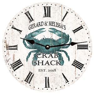 May include: A white wooden clock with Roman numeral markings and a blue crab design. The clock face reads "Gerard & Melissa's Crab Shack Est. 2018".