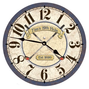 May include: Round wall clock with a distressed cream-colored face, dark brown numerals, and black hands. The clock features crossed golf clubs and the text "Tim's 19th Hole" and "Est. 2020". The outer rim is blue.