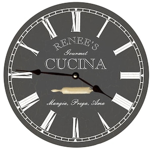 May include: Gray round clock with Roman numeral markings and a rolling pin graphic. The clock face reads "Renee's Gourmet Cucina Mangia, Prega, Ama".