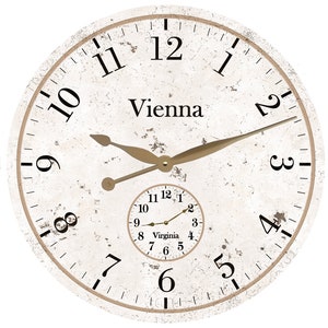 May include: A white, distressed, round clock face with black Roman numeral hour markers and black minute markers. The clock face has a smaller clock face inside with the word "Virginia" and black numbers. The clock hands are gold. The clock face says "Vienna" at the top.