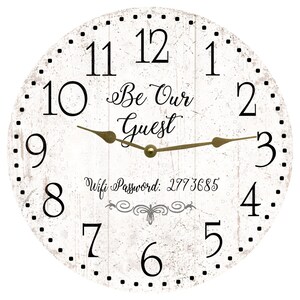 May include: A round wall clock with a white distressed wood-look face, black Arabic numerals, and gold-toned hands. The center features the black text "Be Our Guest" and "Wifi Password: 2773685" above a decorative scroll flourish design.