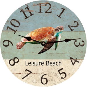 May include: A round wooden clock with a blue and white striped background. A sea turtle is in the center of the clock. The clock face has black Roman numerals and black hands. The text "Leisure Beach" is printed below the turtle.