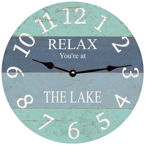 May include: A round wooden clock with a blue and green striped design. The clock face has white numbers and the text "RELAX You're at THE LAKE".