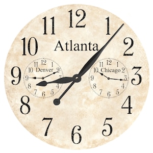 Könnte beinhalten: Ein Vintage-Uhrzifferblatt mit schwarzen Zeigern und römischen Ziffern. Das Uhrzifferblatt ist cremefarben mit einer abgenutzten Textur. Das Uhrzifferblatt zeigt die Zeit in Atlanta, Denver und Chicago an.