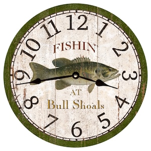 May include: A green and white round wall clock with a large bass fish graphic. The clock face reads "FISHIN AT Bull Shoals" with Roman numeral hour markers.