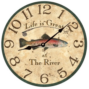 May include: A round, cream-colored clock with a green border. The clock face features a trout, a fishing rod, and the text "Life is Great at The River".