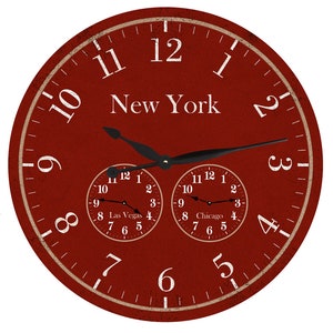 Pode incluir: Um relógio redondo vermelho com ponteiros pretos e números brancos. O mostrador do relógio tem as palavras "New York" em branco. Existem dois relógios menores no mostrador, um rotulado como "Las Vegas" e o outro como "Chicago".