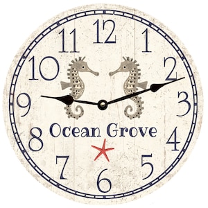 May include: A white round clock with blue Roman numerals and a navy blue outer ring. The clock face features two seahorses facing each other and the text "Ocean Grove" with a red starfish below.