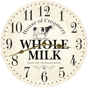 May include: A round clock face with a cream-colored background. The clock features black numbers, a cow illustration, and the words "House of Creamery" and "WHOLE MILK." The clock hands are gold-colored.