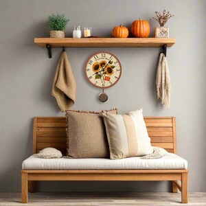 May include: A round wall clock with a sunflower design hangs on a gray wall. The clock has a pendulum and is surrounded by a wooden shelf with decorative items, including pumpkins, candles, and a plant. A wooden bench with pillows is below.