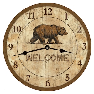 May include: A round wooden clock with a brown bear illustration and the word "WELCOME" in the center. The clock face has Roman numeral markings and a distressed, vintage look.