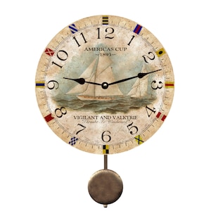 May include: A vintage-style pendulum clock with a nautical theme. The clock face features a sailboat on the water with the text "Americas Cup - 1893 -" and "Vigilant and Valkyrie "Thrasht To Windward". The clock face is surrounded by nautical flags in red, blue, yellow, and white.