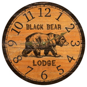 May include: A round wooden clock with black numbers and a black border. The clock face is orange with a black and white illustration of a bear. The text "BLACK BEAR LODGE" is printed on the clock face.