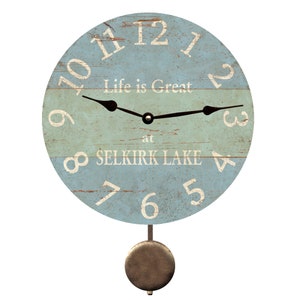 May include: A blue and white wooden pendulum clock with the text "Life is Great at SELKIRK LAKE".