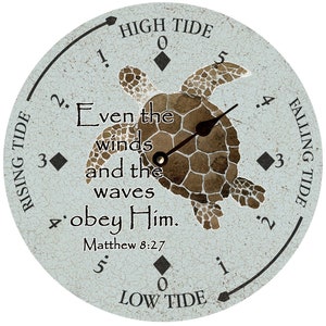 May include: A blue and white round wooden tide clock with a sea turtle design. The clock face has a black hand and a white dial with the words "High Tide", "Low Tide", "Rising Tide", and "Falling Tide". The clock also has the text "Even the winds and the waves obey Him. Matthew 8:27".