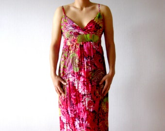 May include: A long, floral-print dress with thin straps. The dress features a V-neckline and a vibrant pattern of pink, green, and purple flowers. The model is wearing red heels.