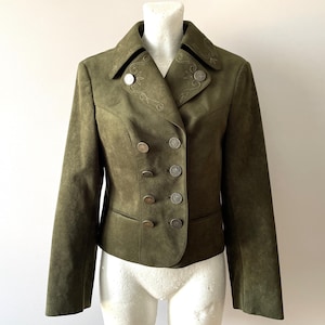 May include: Olive green suede jacket with a double-breasted design. The jacket features decorative embroidery on the collar and silver-toned buttons. The jacket is displayed on a mannequin.