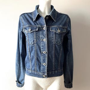 Peut inclure: Une tasse en céramique blanche avec une anse noire et l'inscription "But First, Coffee" en gras noir. La tasse est posée sur un fond flou. La tasse mesure environ 10 cm de hauteur.