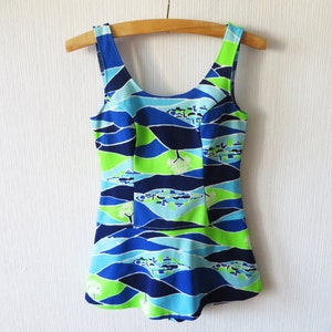 May include: A sleeveless one-piece swimsuit featuring a scoop neckline and a flared skirted bottom. The garment displays a vibrant abstract landscape pattern in shades of navy blue, bright lime green, and light sky blue across the entire surface.