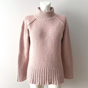 Peut inclure: Un pull rose clair à col roulé sur un mannequin. Le pull à manches longues a des poignets et un ourlet côtelés. Le tricot texturé a un design classique. Le vêtement est présenté sur fond blanc.