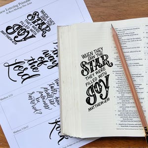 Könnte beinhalten: Ein weißes Blatt Papier mit schwarz gedruckten Schriftzügen mit dem Titel The Book of Matthew Lettering Printable von Reva Madryga Fine Artist, neben einem aufgeschlagenen Buch mit schwarzem Text und einem hellbraunen Stift auf der Seite.
